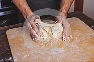 Men`s hands knead dough on the table in the kitchen
