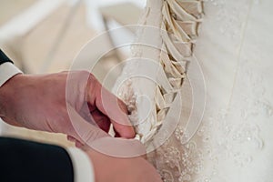 Men& x27;s hands lace up corset on the bride& x27;s dress, close up