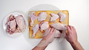 men's hands lay out a butchered carcass of raw chicken on a wooden cutting board