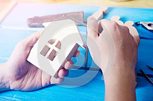 Men`s hands make a hand-made article of wood on the background of a blue table with tools. Work at home and in the workshop.