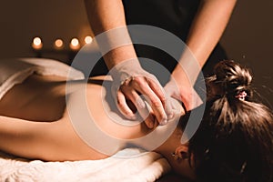 Men`s hands make a therapeutic neck massage for a girl lying on a massage couch in a massage spa with dark lighting