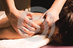 Men`s hands make a therapeutic neck massage for a girl lying on a massage couch in a massage spa with dark lighting