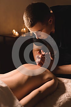 Men`s hands make a therapeutic neck massage for a girl lying on a massage couch in a massage spa with dark lighting