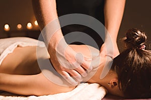 Men`s hands make a therapeutic neck massage for a girl lying on a massage couch in a massage spa with dark lighting