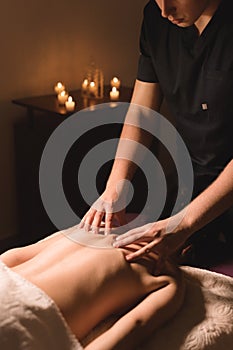 Men`s hands make a therapeutic neck massage for a girl lying on a massage couch in a massage spa with dark lighting