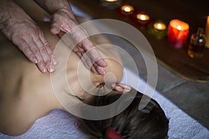 Men`s hands make a therapeutic neck massage for a girl lying on a massage couch in a massage spa with dark lighting