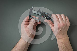 Men's hands measure the screw using an electronic caliper