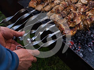 Men`s hands overturn skewers with meat roasted