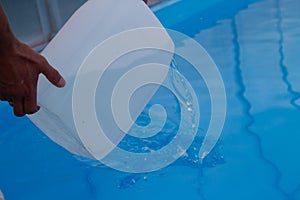 Men`s hands pour light liquid from a plastic tank into a pool, into water. chemical water purification, alkali balance, unsanitar