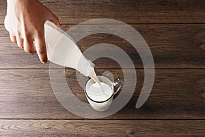 Men`s hands pour milk from a bottle into a glass, close-up, top view. Brown wooden table