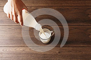 Men`s hands pour milk from a bottle into a glass, close-up, top view. Brown wooden table