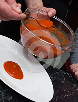 Men`s Hands Pouring Red Tomatoe or Chilly Sauce over Red Plate for Food Garnish. Ketchup Spill of Tomato sauce. Vertical