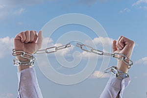 Men`s hands in a shirt break chains against the background of the sky and clouds., color illumination. Concept: freedom of the ind