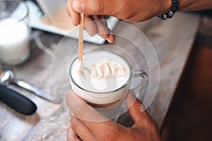 Men`s hands stir a latte in a glass with a stick