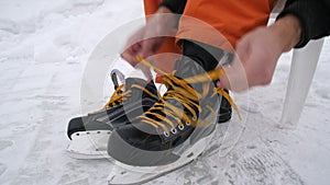 Men's hands tighten the laces on skates. Hockey skates with bright yellow laces. Preparing for skiing on snow-covered