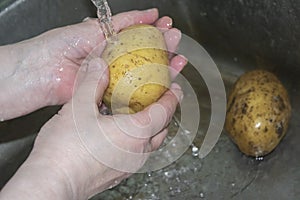 Men`s hands wash under running water uncleaned potatoes. Home cooking. Close up