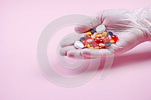 Men`s hands in white rubber gloves hold many multi-colored pills on a pink background