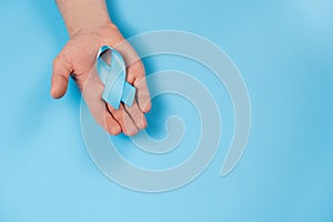 Men`s health and Prostate cancer awareness campaign concept. Male hand holding blue ribbon awareness on color background wall in