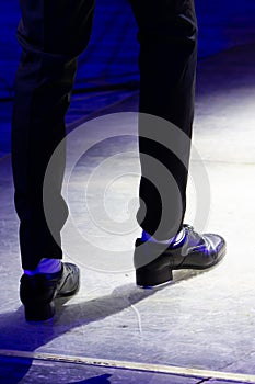 Men's legs in motion in stage trousers with stripes and leather shoes for Irish dancing on the floor