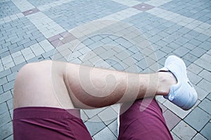 Men`s legs in shorts and white sneakers in the park on the alley. leg on foot.