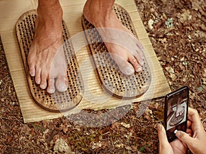 Men& x27;s legs stand on two boards with sharp spikes and women& x27;s hands take photos on the phone. Sadhu board