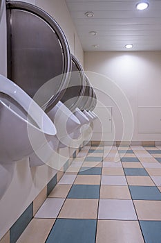 Men`s public restroom with urinals on the wall and checkered floor.