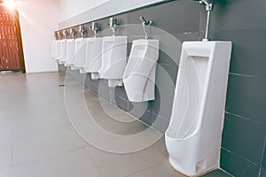 Men`s room with white porcelain urinals in line. Modern clean public toilets with tiles