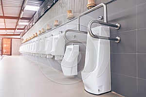 Men`s room with white porcelain urinals in line. Modern clean public toilets with tiles
