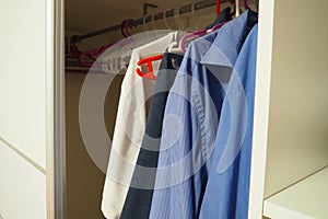 Men& x27;s shirts hang on hangers in an open white closet. Men& x27;s fashion. Organization of things in a closet or
