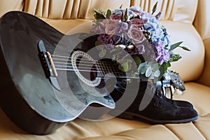 Men`s shoes, a guitar and a bouquet are on a leather sofa