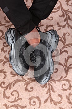 Men`s tanned legs in black fashionable sneakers. An unrecognizable photo. Just my legs. Copy of the space. Vertical photo.Top vie