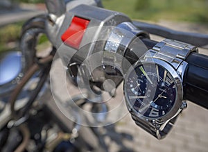 Men`s watches with two dials and an iron bracelet hang on the throttle handle of a chopper motorcycle