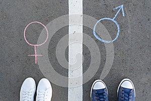 Men`s and women`s feet on the asphalt in front of gender symbols