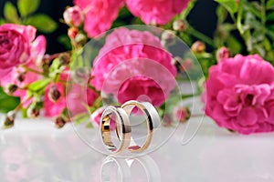 Men's and women's wedding rings and roses on background.