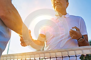 Men shaking hands while standing by tennis net against clear sky on sunny day