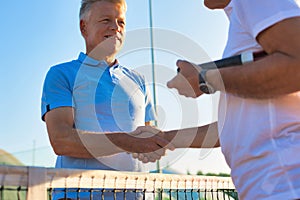 Men shaking hands while standing by tennis net against clear sky on sunny day