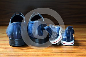 Men shoes and children sneakers side by side on the wooden floor