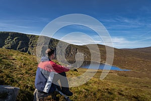 Men sitting on a rock and drinking coffee from thermos. Scenic view on Lough Ouler and Tonelagee Mountain, Ireland