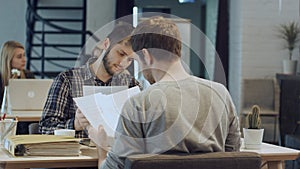 Men are sitting at table in modern offce and shaking hands, making agreement