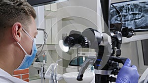 Men specialist works with optical microscope in front of jaw on monitor in dentist`s office