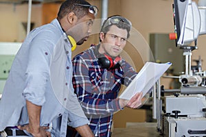 men stood by factory equipment looking at paperwork