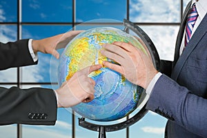 Men studying globe near window.