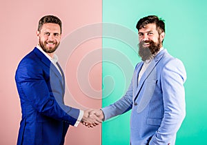 Men in suits businessmen hold hands in handshake. Businessmen with unshaven smiling faces shaking hands pink background