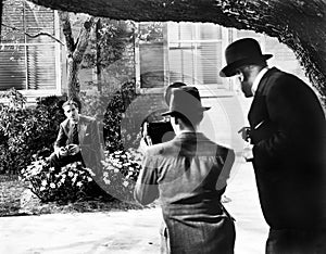 Men taking a picture of a man sitting in flower bed