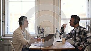 Men talking and recording business podcast, sitting at table in front of microphones in studio spbd.