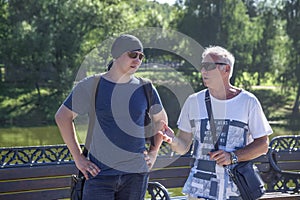 Men of two generations in informal clothes are having a conversation in a city park on a summer day