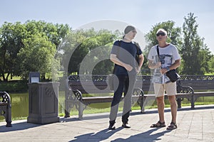 Men of two generations in informal clothes are having a conversation in a city park on a summer day