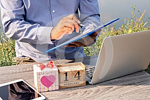 Men use a natural cave laptop with a heart-shaped gift box and wooden calendar. Concept of love, holiday, valentine`s day