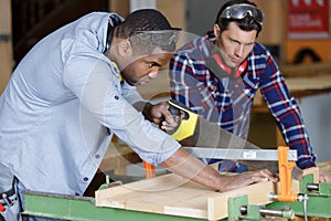 men using hand saw to cut wood in woodshop photo