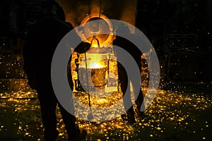 Men watching sparkling melting steel in furnace of foundry.